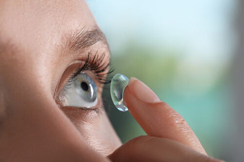 Young woman putting contact lens her eye blurred background closeup